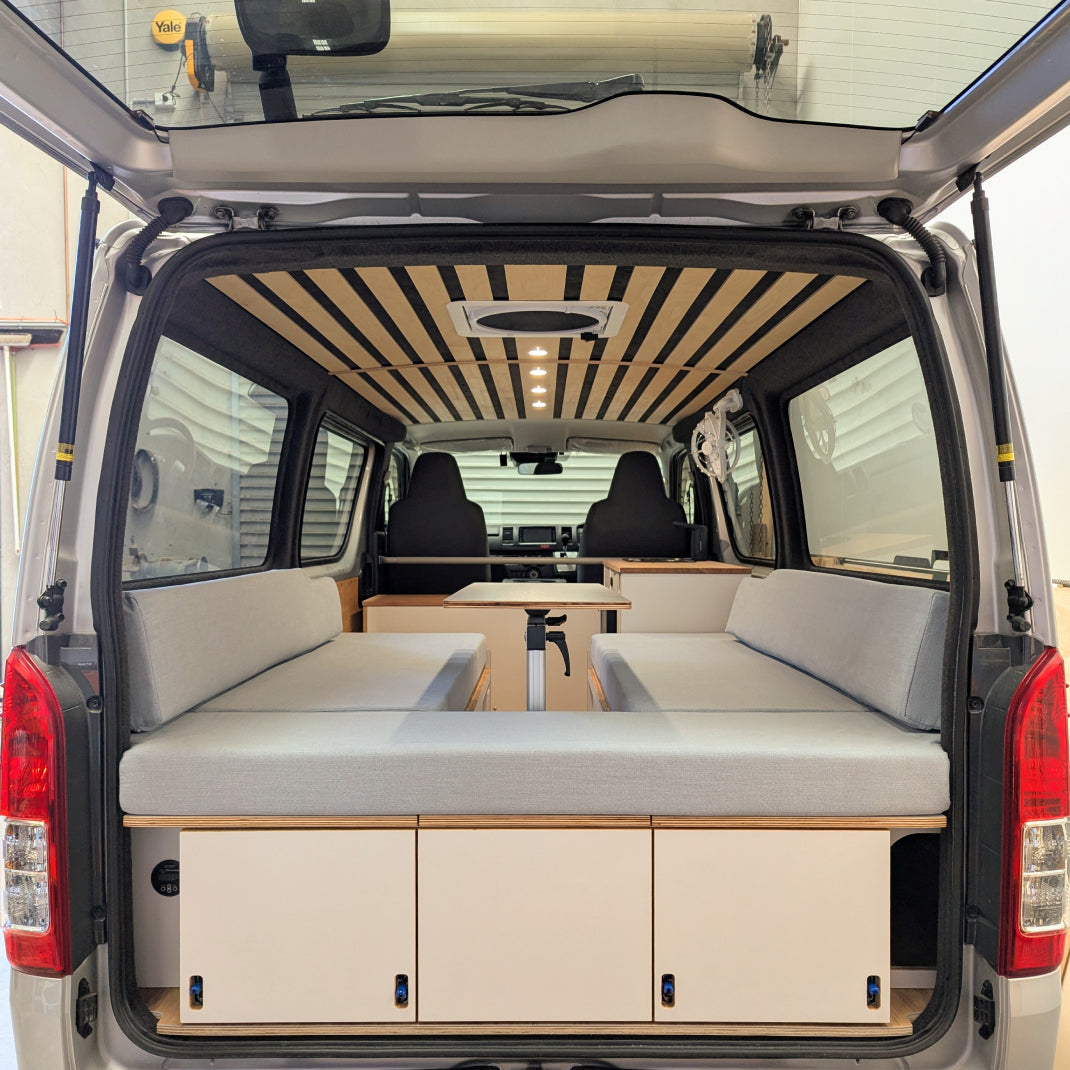 HiAce interior with bed in day mode, storage drawers, and custom Birch ceiling.